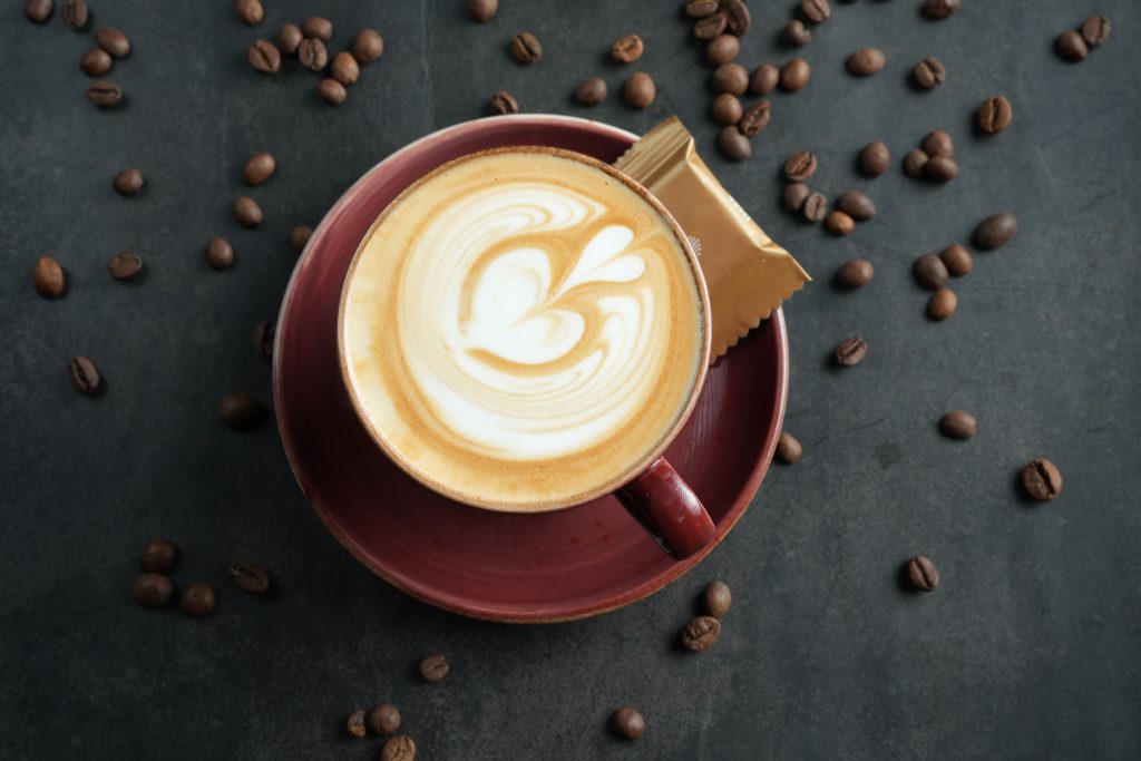 Top view of a latte with beautiful latte art, surrounded by coffee beans on a dark surface.