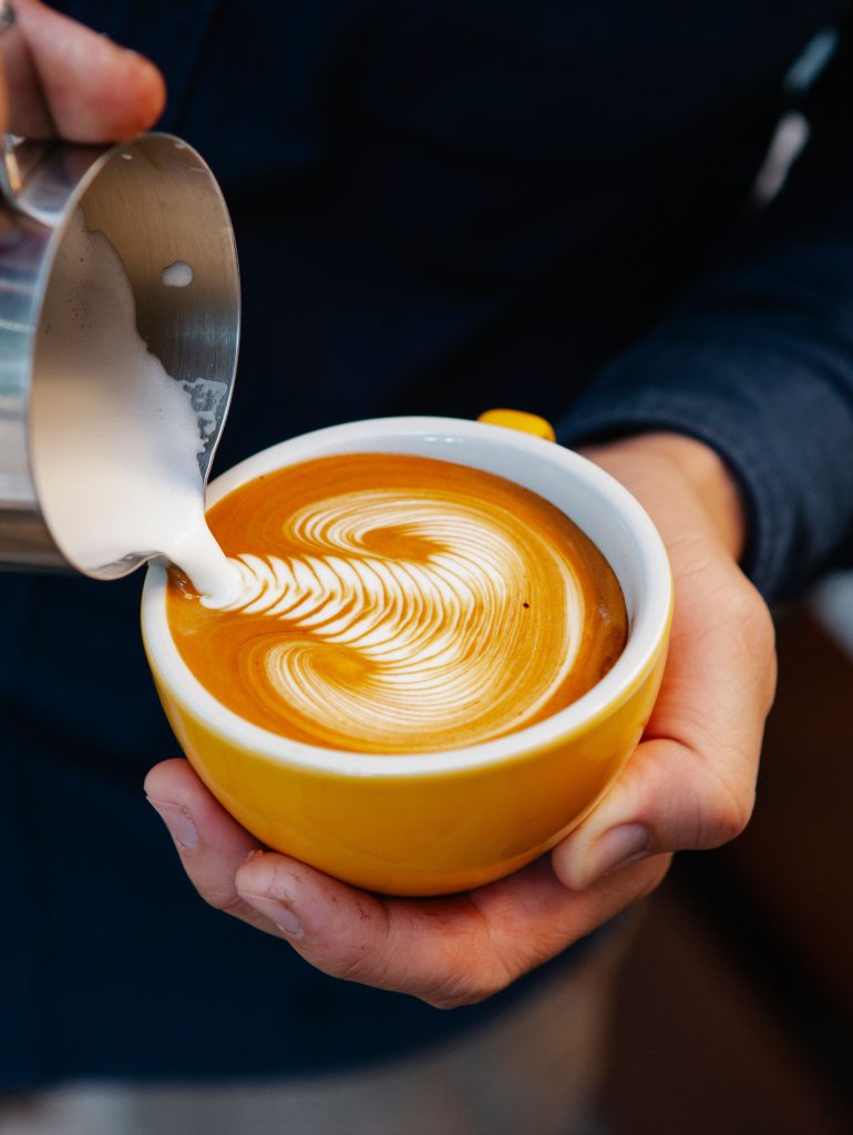 From above of crop anonymous male pouring cream into mug with coffee while making latte art